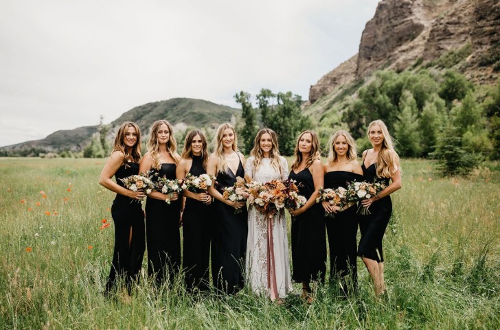 bridal party standing in a field wearing black bridesmaid dresses purchased online from Revolve