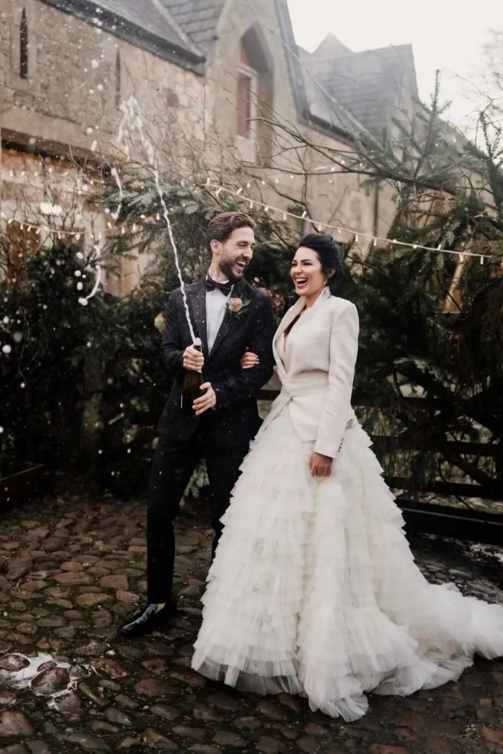 couple popping champagne in the winter wonderland snow best Christmas wedding ideas
